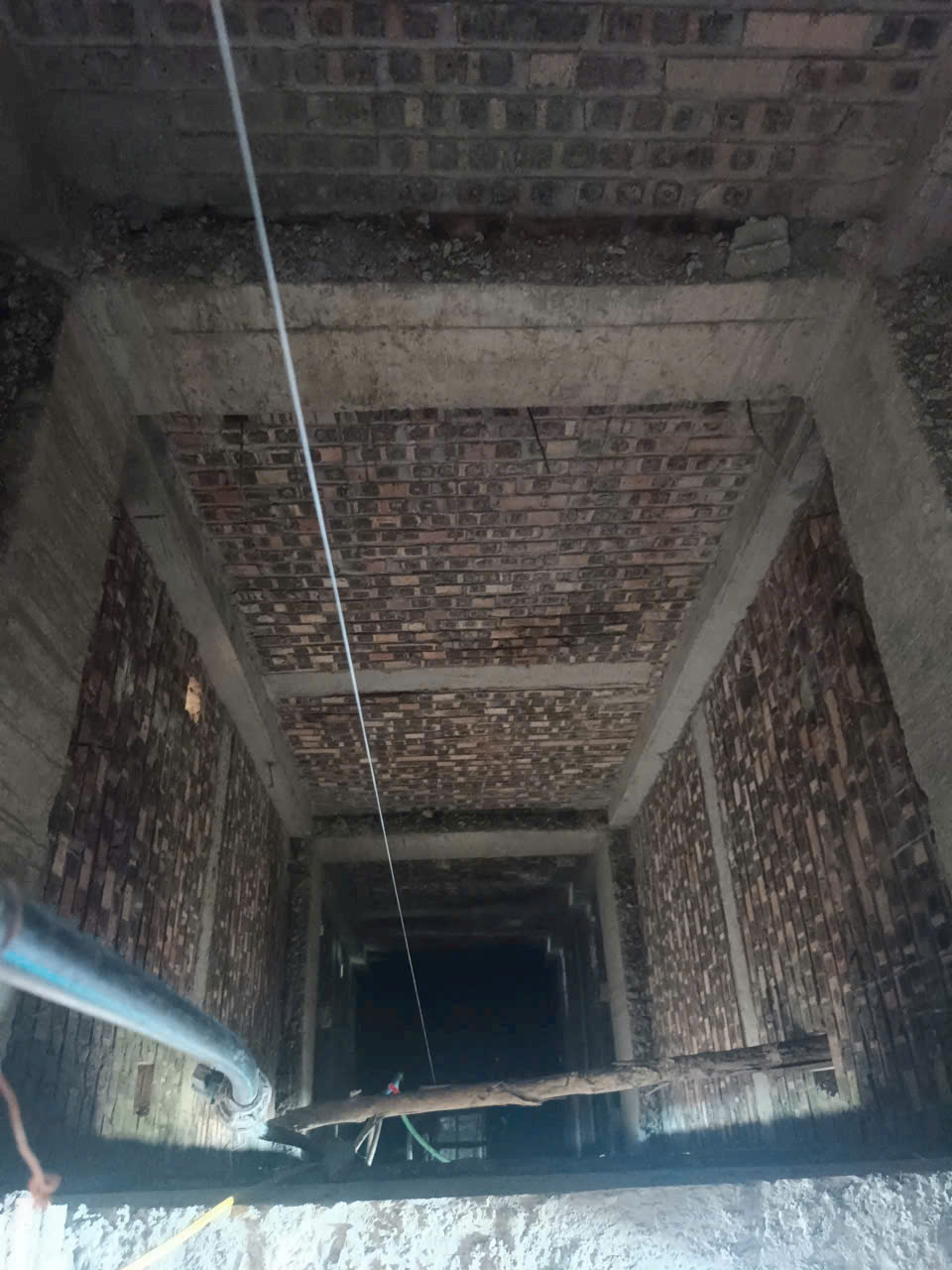 Hố thang máy xây gạch đang thi công với hệ thống ống kỹ thuật chạy dọc bên trong